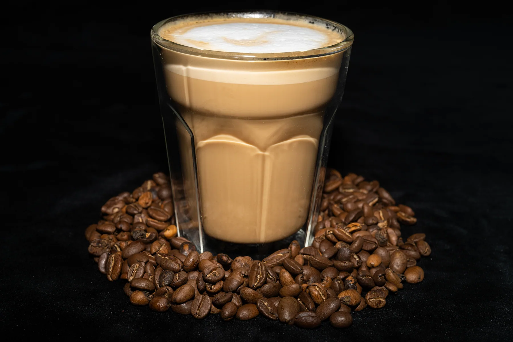 Latte in a glass photographed with coffee beans